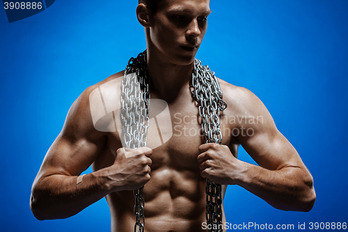 Image of Muscular guy with chains on his shoulders against a blue wall