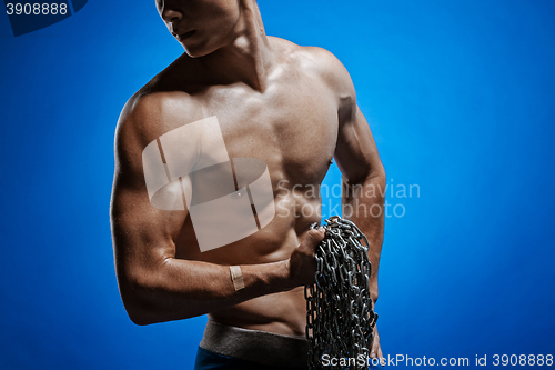 Image of Muscular guy with chains on his shoulders against a blue wall