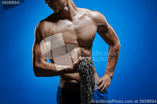 Image of Muscular guy with chains on his shoulders against a blue wall
