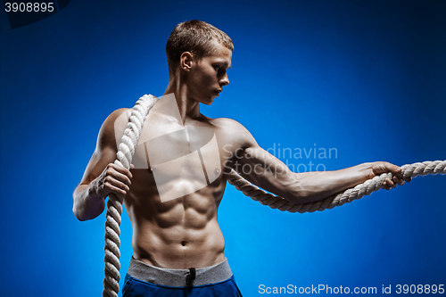 Image of Fit young man with beautiful torso and a rope on blue background