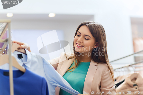 Image of happy young woman choosing clothes in mall