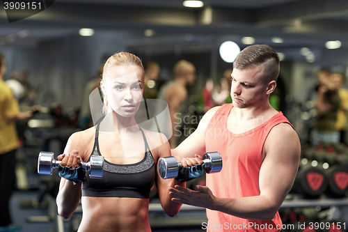 Image of young couple with dumbbells flexing muscles in gym