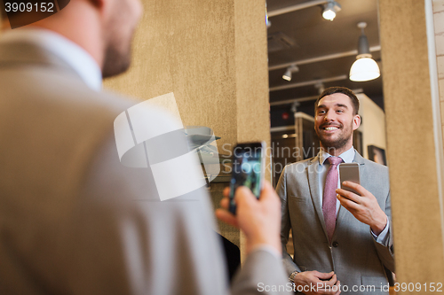 Image of man in suit taking mirror selfie at clothing store