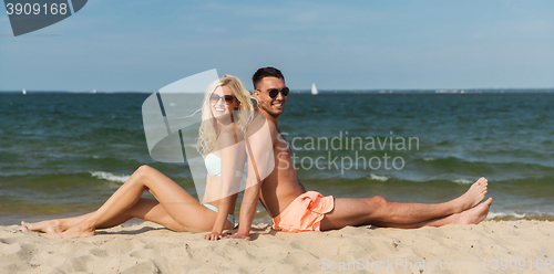 Image of happy couple in swimwear sitting on summer beach