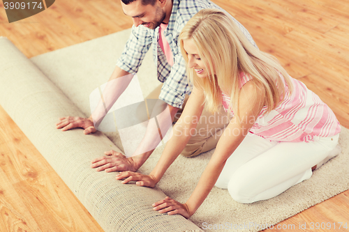 Image of happy couple unrolling carpet or rug at home