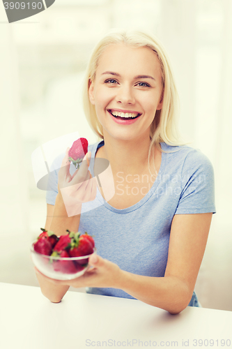 Image of happy woman eating strawberry at home