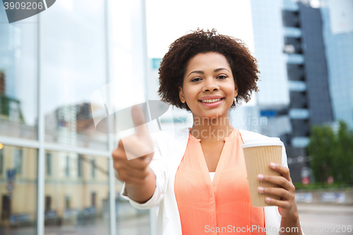 Image of happy woman with coffee showing thumbs up in city
