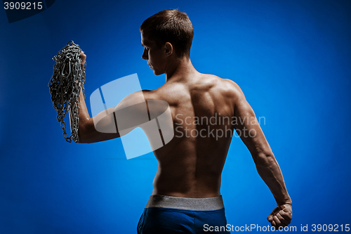 Image of Muscular guy with chains on his shoulders against a blue wall