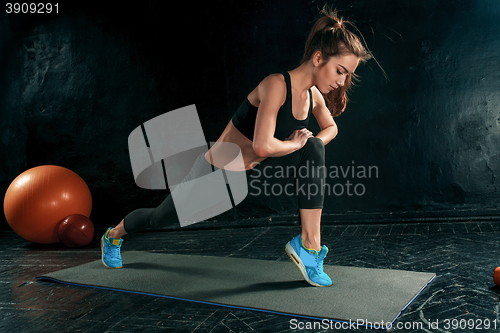 Image of Beautiful slim brunette doing some stretching exercises in a gym