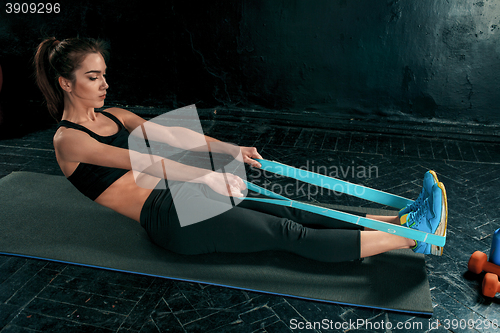 Image of The brunette athletic woman exercising with rubber tape