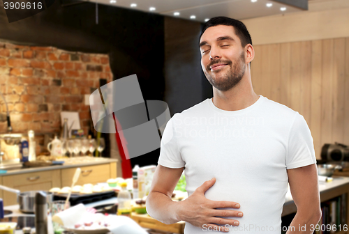 Image of happy full man touching tummy over kitchen