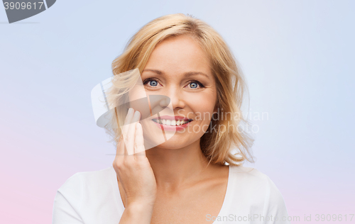 Image of smiling woman in white t-shirt touching her face