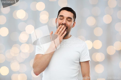 Image of yawning man over holidays lights background