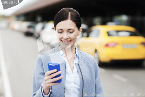 Image of smiling woman with smartphone over taxi in city