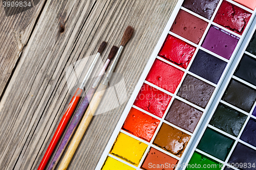 Image of paint-box and three brushes on a textured surface