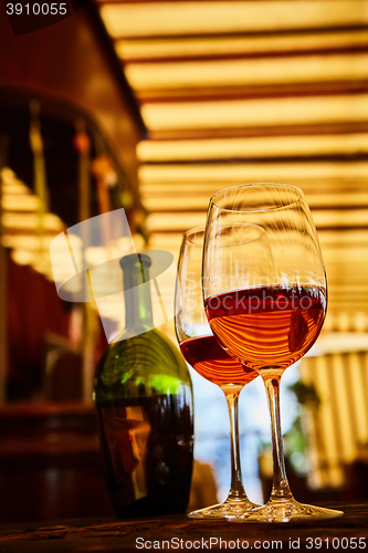 Image of two glasses filled with red wine and bottle in background