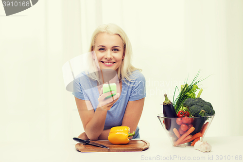 Image of smiling woman with smartphone cooking vegetables