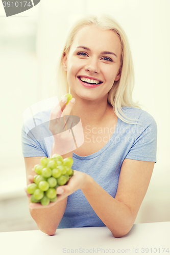 Image of happy woman eating grapes at home