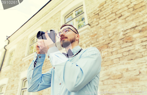 Image of happy young hipster man with film camera in city