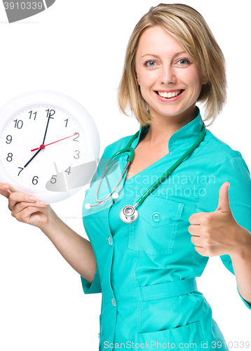 Image of Young lady doctor is holding clock showing seven