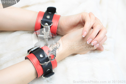 Image of female hands in leather handcuffs. on the background sheet. sex toys.