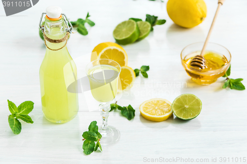 Image of Home lime liquor in a glass and fresh lemons, limes on the white wooden background