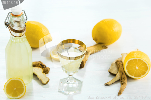 Image of Home ginger tincture in a glass and fresh lemons on the white wooden background