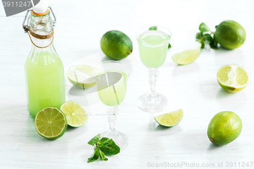 Image of Home lime liquor in a glass and fresh lemons and limes on the white wooden background