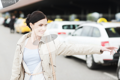 Image of smiling young woman waving hand and catching taxi