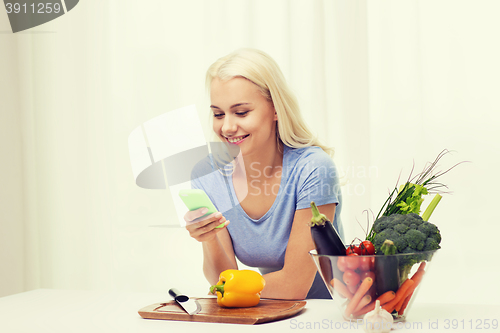 Image of smiling woman with smartphone cooking vegetables