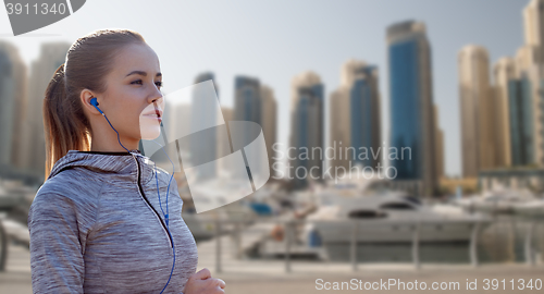 Image of happy woman with earphones running over dubai city