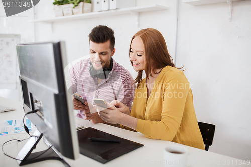 Image of happy creative team with smartphones at office