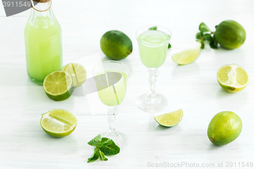 Image of Home lime liquor in a glass and fresh lemons, limes on the white wooden background