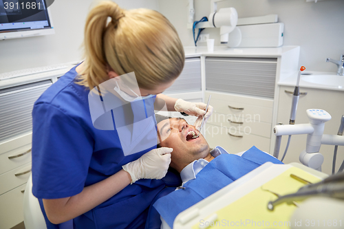Image of female dentist checking up male patient teeth
