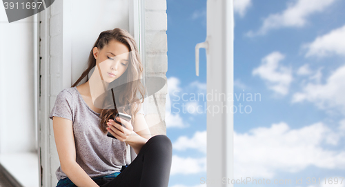 Image of sad pretty teenage girl with smartphone texting