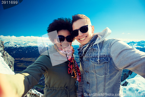 Image of happy teenage couple taking selfie over mountains