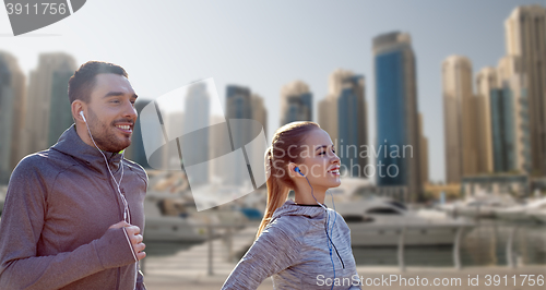 Image of happy couple with earphones running in city