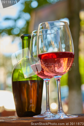 Image of two glasses filled with red wine and bottle in background