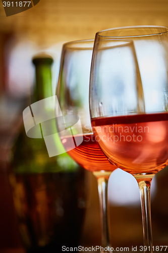 Image of two glasses filled with red wine and bottle in background