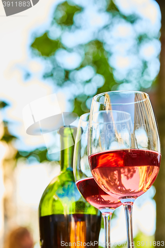 Image of two glasses filled with red wine and bottle in background