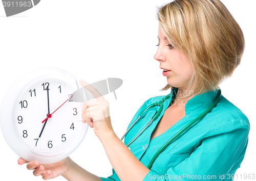 Image of Young lady doctor is holding clock showing seven