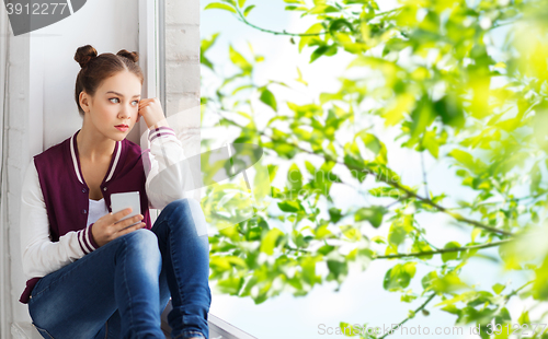 Image of teenage girl sitting on windowsill with smartphone