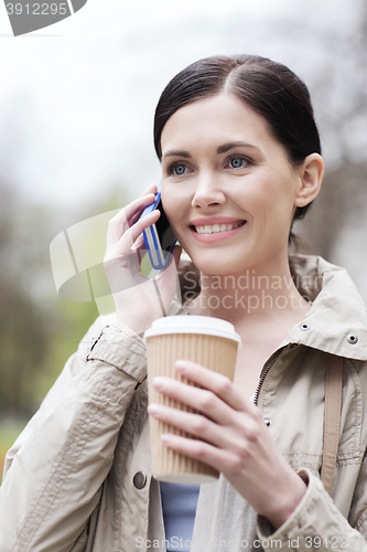 Image of smiling woman with smartphone and coffee in park