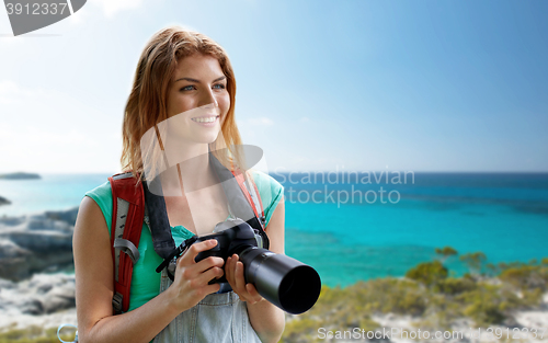 Image of happy woman with backpack and camera over seashore