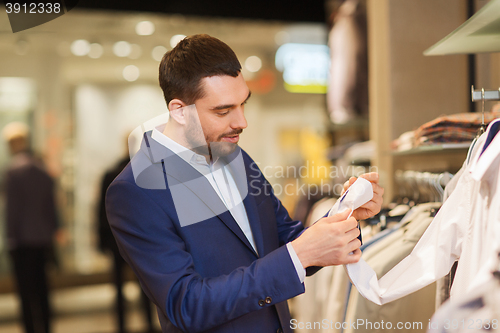 Image of happy young man choosing clothes in clothing store