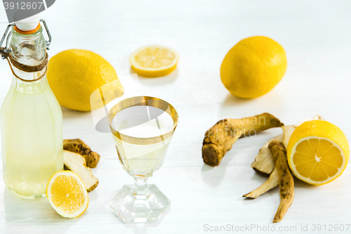 Image of Home ginger tincture in a glass and fresh lemons on the white wooden background