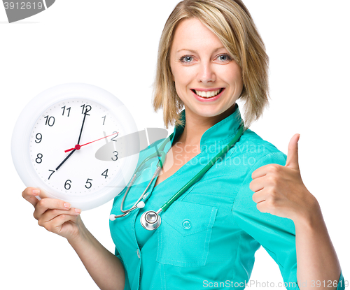 Image of Young lady doctor is holding clock showing seven