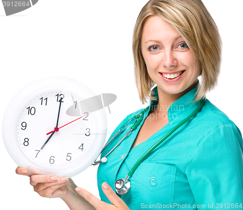 Image of Young lady doctor is holding clock showing seven