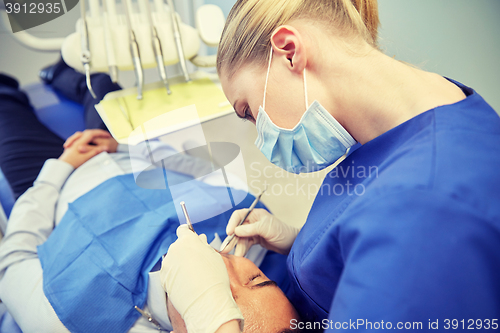 Image of female dentist in mask checking male patient teeth