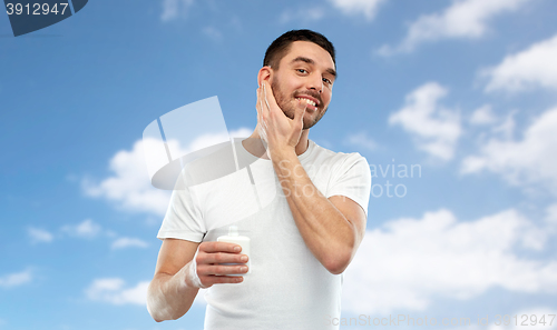 Image of happy young man applying cream or lotion to face